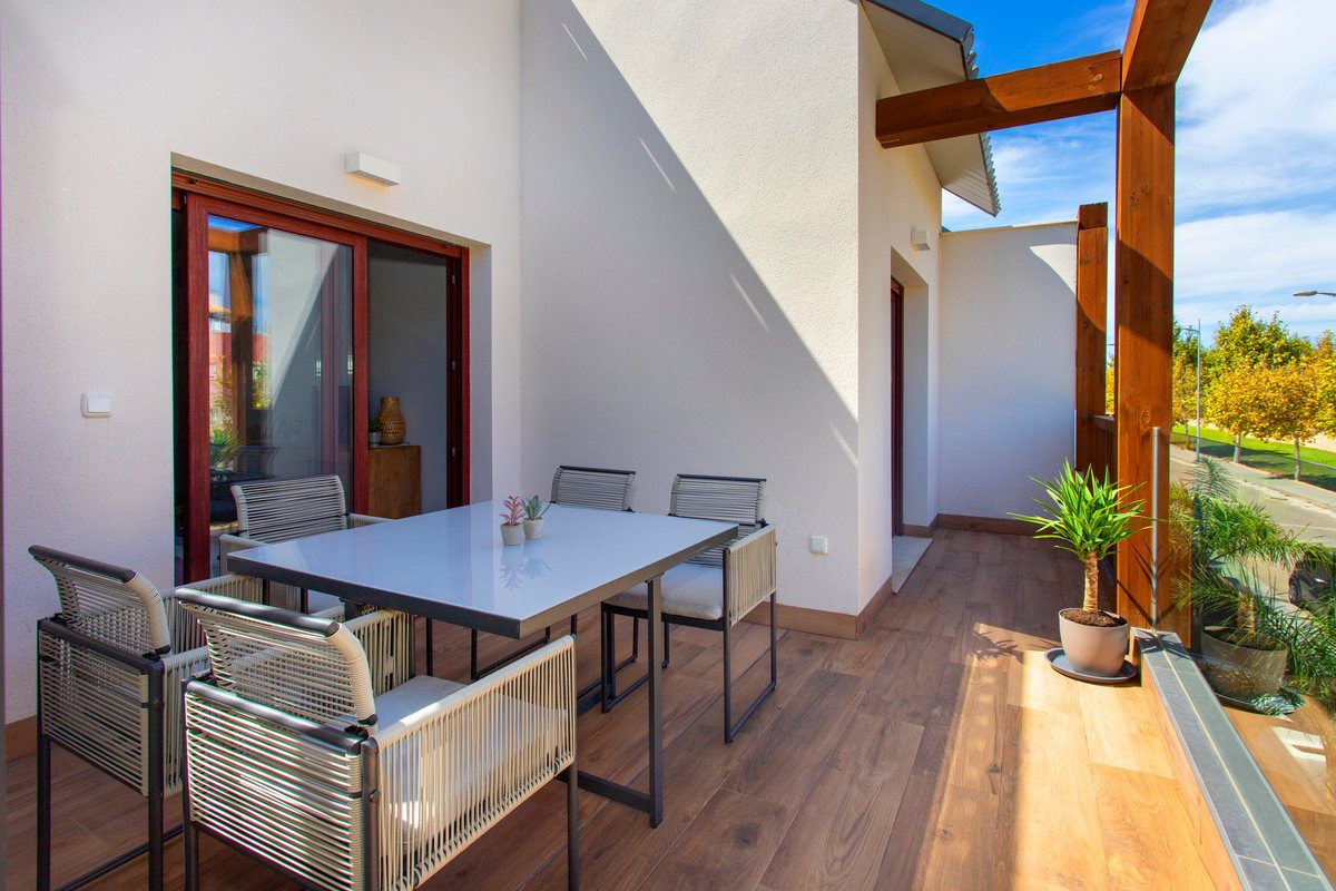 Balcony with table and chairs by the sliding door, with a plant in the sun