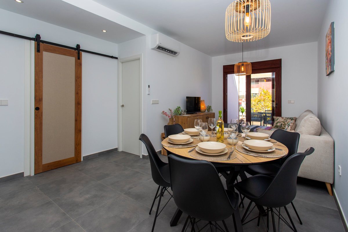 Round dining table for six, laid under a rattan pendant light, with the sliding door to the bathroom