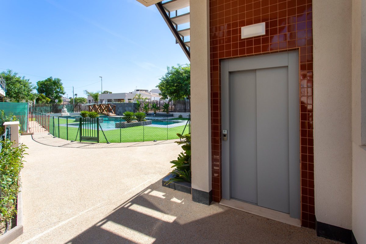 The lift at the building entrance, with the fenced garden and pool behind it
