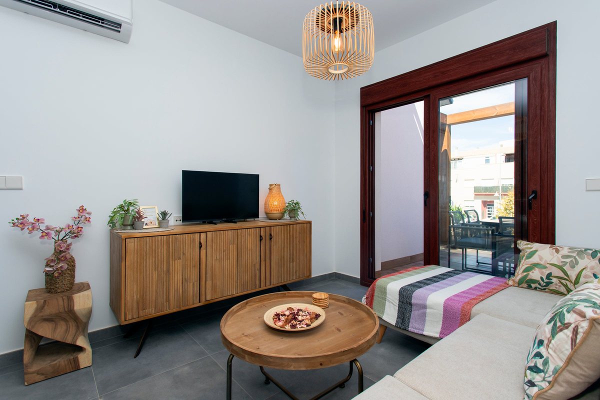 Living room with a TV on a wooden sideboard, a round coffee table and the door to the balcony