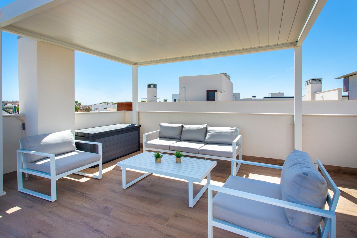 Lounge sofas and a coffee table under the white pergola on the roof terrace, overlooking the rooftops of Pilar de la Horadada