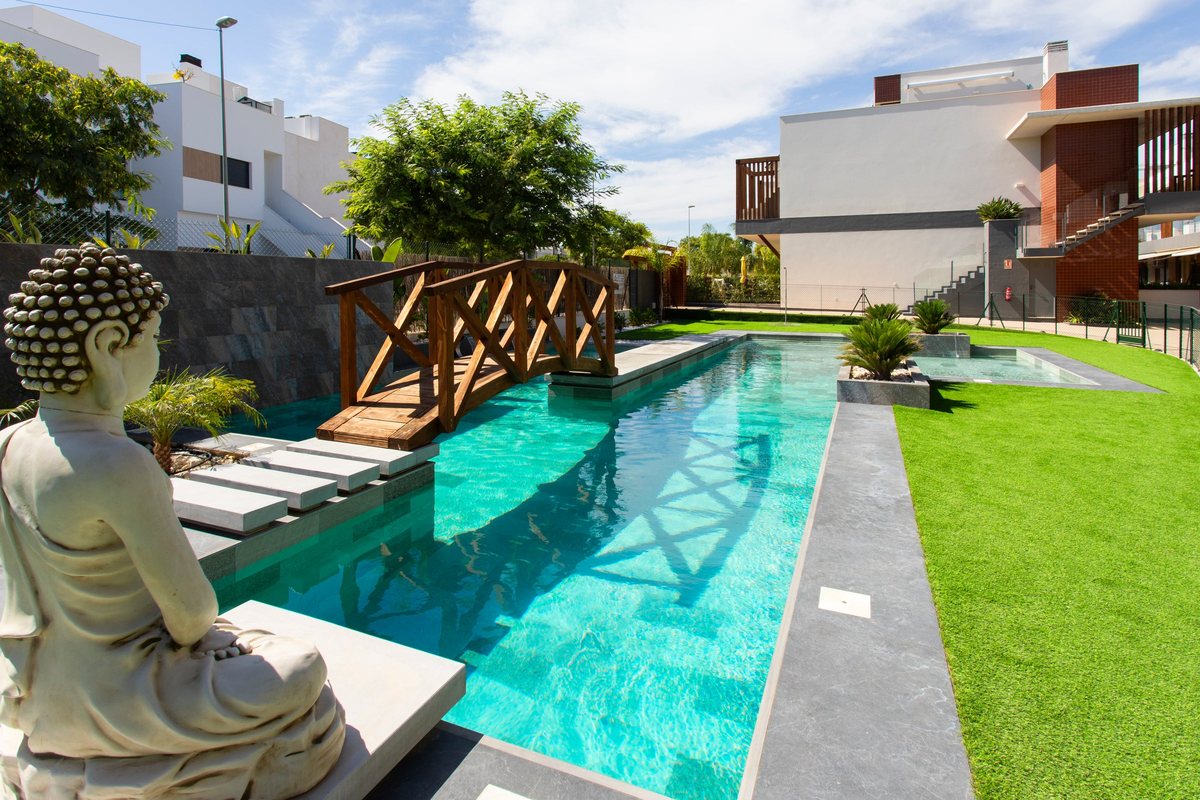 The zen-style pool of the complex with a Buddha statue, a wooden bridge and palm trees